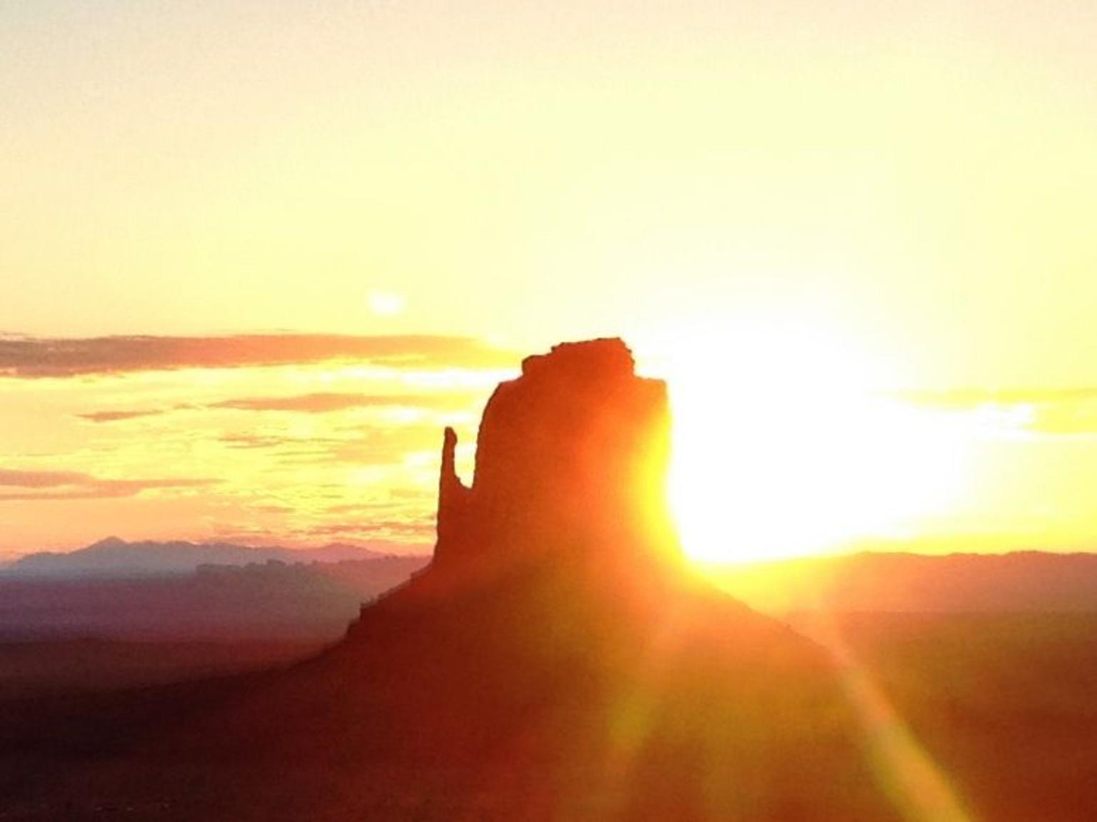 the sun rising behind Monument Valley